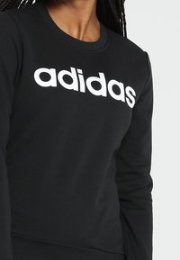 Sweatshirt noir en mélange de coton, avec un col rond et des manches longues. Logo "adidas" blanc imprimé en évidence sur la poitrine.