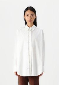 White, button-up shirt with a classic collar, long sleeves, and a loose fit. Smooth cotton fabric with a clean, minimalist design.