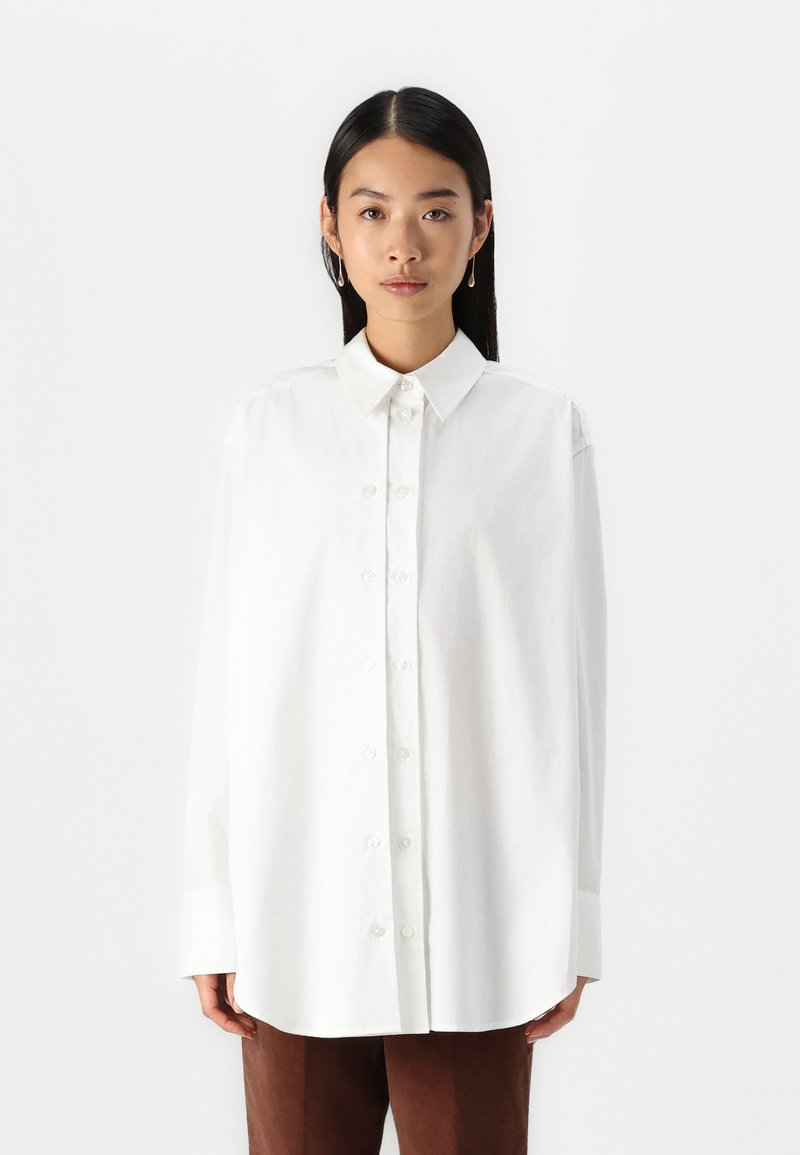 White, button-up shirt with a classic collar, long sleeves, and a loose fit. Smooth cotton fabric with a clean, minimalist design.