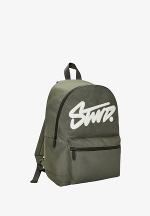 Zielona oliwkowa plecak z tkaniny o zaokrąglonym topie, z przednią kieszenią na zamek błyskawiczny oraz białym haftowanym logo. Posiada regulowane paski i pętelkę do zawieszenia.