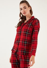 Crvene flanel onesie pidžame s crnim i bijelim kariranim uzorkom. Ima gornji dio s dugmadi i ovratnikom, te hlače s odgovarajućim uzorkom. Mekana tekstura.