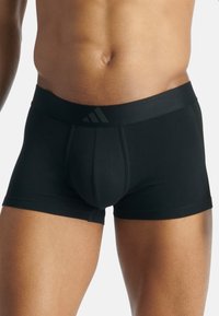 Svarta boxershorts i ett slätt material, med ett svart midjeband som har tre ränder logotyp och en konturerad framficka för stöd.