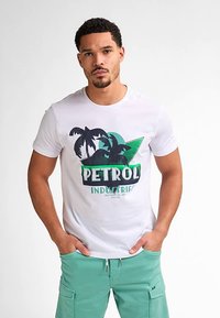 Bílé bavlněné tričko se zeleno-černým grafickým potiskem palm a nápisem "PETROL INDUSTRIES", doplněné mintově zelenými šortkami.