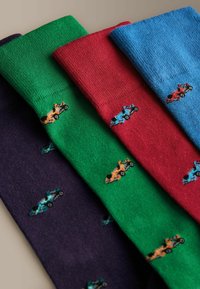 Quatre chaussettes pliées en bleu marine, vert, rouge et bleu avec de petits motifs brodés de voitures de course dispersés sur chaque chaussette.