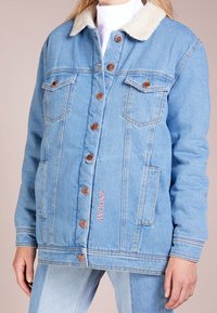 Ljusblå denimjacka med en beige sherpa-krage, kopparknappar, två bröstfickor, sidofickor och broderad "2ND DAY" detalj.