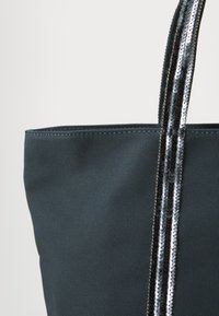 Sac fourre-tout vert foncé avec un tissu texturé et deux anses en sequins noirs brillants. Le sac a un design simple et des bords droits.