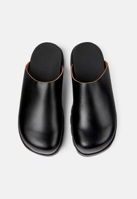 Mules en cuir noir avec une finition lisse, dos ouvert et bout arrondi. Subtils accents marron et semelles texturées. Logo embossé sur les semelles.