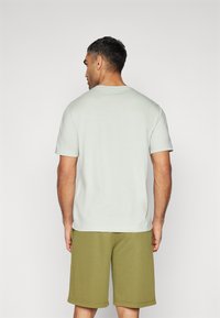 Hellgrünes T-Shirt mit kurzen Ärmeln und rundem Ausschnitt. Kombiniert mit olivgrünen Shorts, beide aus weichem, glattem Stoff.