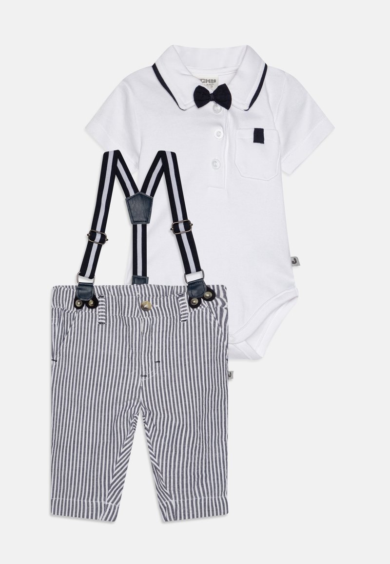 Bela kratka majica z ovratnikom in temnim metuljčkom, v kombinaciji z mornarsko modrimi in belimi črtastimi hlačami ter nastavljivimi črnimi naramnicami.