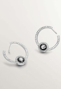 Pendientes de aro plateados con una superficie brillante, adornados con piedras de imitación claras y una piedra negra central, que presentan un diseño circular.
