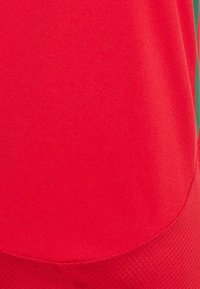 Camiseta atlética roja con una textura suave, dobladillo redondeado y sección inferior con patrón. Confeccionada con material ligero y transpirable.