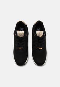 Black athletic shoes made of mesh fabric with gold accents, round laces, and a padded tongue. Features a white outsole and logo detail.