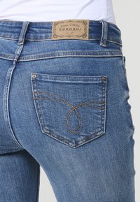 Vaqueros de mezclilla con un lavado azul claro, que cuentan con una etiqueta de marca de cuero en la parte trasera y un bordado intrincado en el bolsillo trasero.