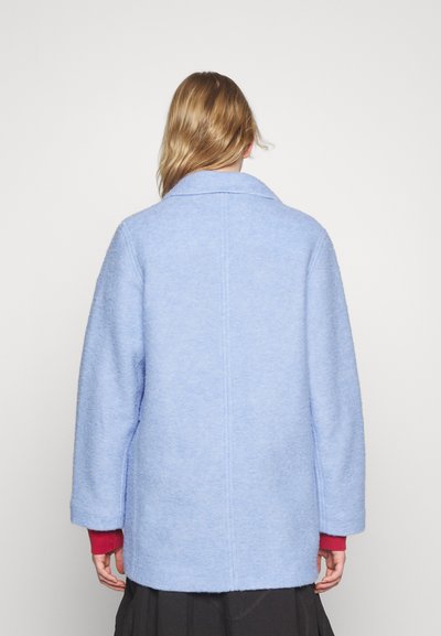 Manteau en laine bleu clair avec un col cranté, des épaules tombantes et de longues manches. Présente une coupe droite et un tissu texturé.