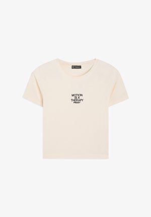 T-shirt a maniche corte con scollo rotondo in tessuto beige chiaro con testo ricamato nero "MOTION IS A THERAPY" centrato sul davanti.