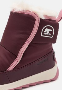 Botte imperméable bourgogne avec doublure en fausse fourrure rose douce. Comprend le logo Sorel, des accents cousus et une semelle en caoutchouc texturé pour plus d'adhérence.