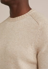 Béžový pletený svetr s kulatým výstřihem, strukturovaným vzorem a raglánovými rukávy, vyrobený z měkkého a lehkého materiálu.
