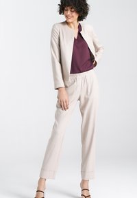 Beżowa marynarka o dopasowanym kroju z okrągłym dekoltem, w połączeniu z głęboko bordową bluzką i jasnobeżowymi spodniami na gumce.