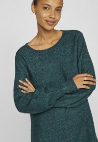 Maglione lavorato a maglia verde smeraldo con una vestibilità ampia, scollo rotondo largo e maniche lunghe con polsini a coste e finitura texturizzata.