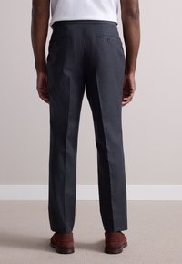 Dark gray trousers with a smooth texture, tailored fit, and two back pockets with button closures. Worn with brown suede shoes.