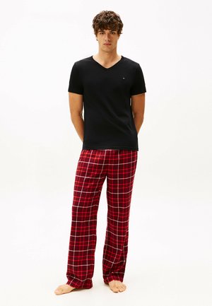 Black short-sleeve V-neck T-shirt paired with red plaid pajama pants featuring white and gray lines, all in a soft fabric. Barefoot.