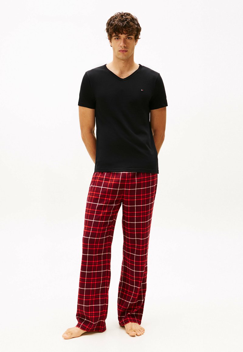Camiseta negra de manga corta con escote en V combinada con pantalones de pijama a rayas rojas con líneas blancas y grises, todo en una tela suave. Descalzo.