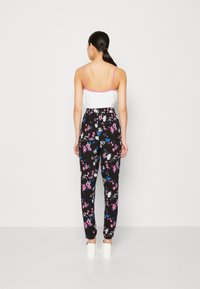 Pantalones negros con estampado de flores multicolores; diseño de cintura alta, cinturilla elástica y perneras ajustadas, combinados con una blusa sin mangas blanca.