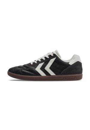 Schwarzer Sneaker mit niedrigem Profil, weißen Chevron-Streifen, weißen Schnürsenkeln, gepolstertem Kragen und brauner Sohle mit "hummel"-Markenaufdruck an der Seite.