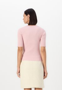 Ljusrosa ribbad stickad topp med korta ärmar, i kombination med en texturerad krämfärgad kjol. Toppen har en rund halsringning och en figurnära design.