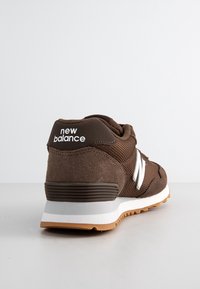 Baskets New Balance marron avec logo "N" blanc et semelle intermédiaire blanche, inclinées pour montrer l’arrière et le côté sur fond blanc uni.