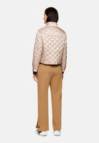 Hellbeige gesteppte Jacke mit cropped Design und hohem Kragen, kombiniert mit braunen Hosen und weißen Sneakern. Schwarze Akzente an den Bündchen.