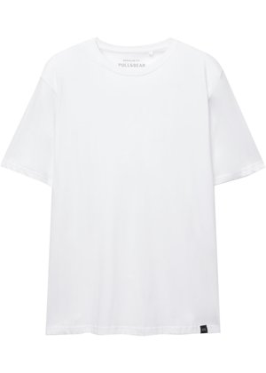 Fehér, rövid ujjú, normál szabású póló kerek nyakkivágással és kis fekete szövettaggal az alsó szélén.