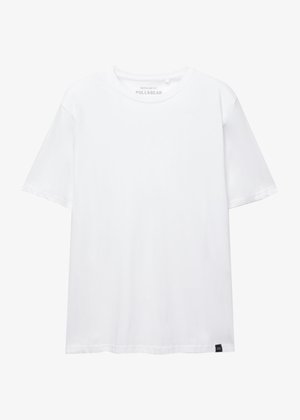 Fehér, rövid ujjú, normál szabású póló kerek nyakkivágással és kis fekete szövettaggal az alsó szélén.