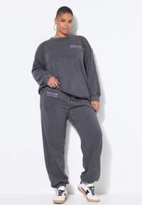 Grijze sweatoutfit met een losse crewneck sweatshirt en taps toelopende broeken. Geborduurde logo's in contrasterende kleuren. Sneakers maken de look compleet.