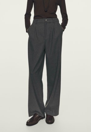 Pantalons rayés gris à taille haute, jambes larges, plis avant et poches latérales. Accompagnés de chaussures marron.