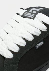 Schwarzer Etnies-Sneaker mit dicken weißen Schnürsenkeln und gebrandeten Stoffetiketten an der Zunge und der Seitenwand.