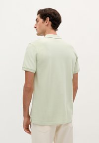 Camisa polo verde claro hecha de un tejido suave, con un cuello clásico y mangas cortas, combinada con pantalones de color claro.