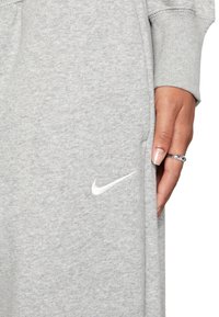 Grau melierte Stoff-Sweatpants mit einem weißen Nike-Logo an der Seite und einer Hand, die den Stoff in der Nähe einer Tasche hält.