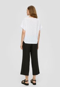 T-shirt en lin blanc avec une coupe ample et des manches retournées, associé à un pantalon noir à jambes larges et des sandales noires à lanières.