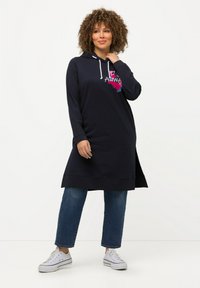 Abito con cappuccio navy a maniche lunghe, con cordini bianchi e grafica colorata "ALWA". Indossato sopra jeans cropped azzurri chiari e sneakers bianche.