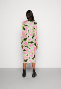 Robe à manches longues avec un motif abstrait multicolore de rose, vert et noir. Le tissu est lisse ; longueur mi-mollet. Bottines noires visibles.