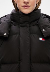 Μαύρο φούτερ μπουφάν με ψηλό γιακά, κουμπιά σνάπ και μια μικρή κόκκινη, λευκή και μπλε λογότυπο ετικέτα στο μπροστινό μέρος.