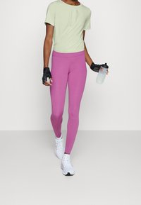Sportliches Outfit mit einem hellgrünen kurz geschnittenen Shirt und pinken Leggings, ergänzt durch eine Wasserflasche und fingerlose Handschuhe, kombiniert mit weißen Schuhen.
