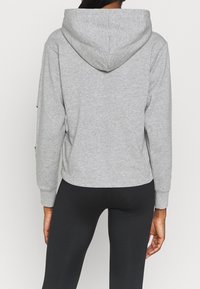 Felpa grigia con cappuccio, maniche lunghe, polsini e orlo a coste, texture morbida e vestibilità rilassata, abbinata a leggings neri.