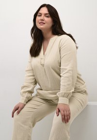 Beige, strukturiertes Loungewear-Set mit einem langärmligen V-Ausschnitt-Oberteil und elastischen Bündchen, kombiniert mit passenden, taillierten Hosen.
