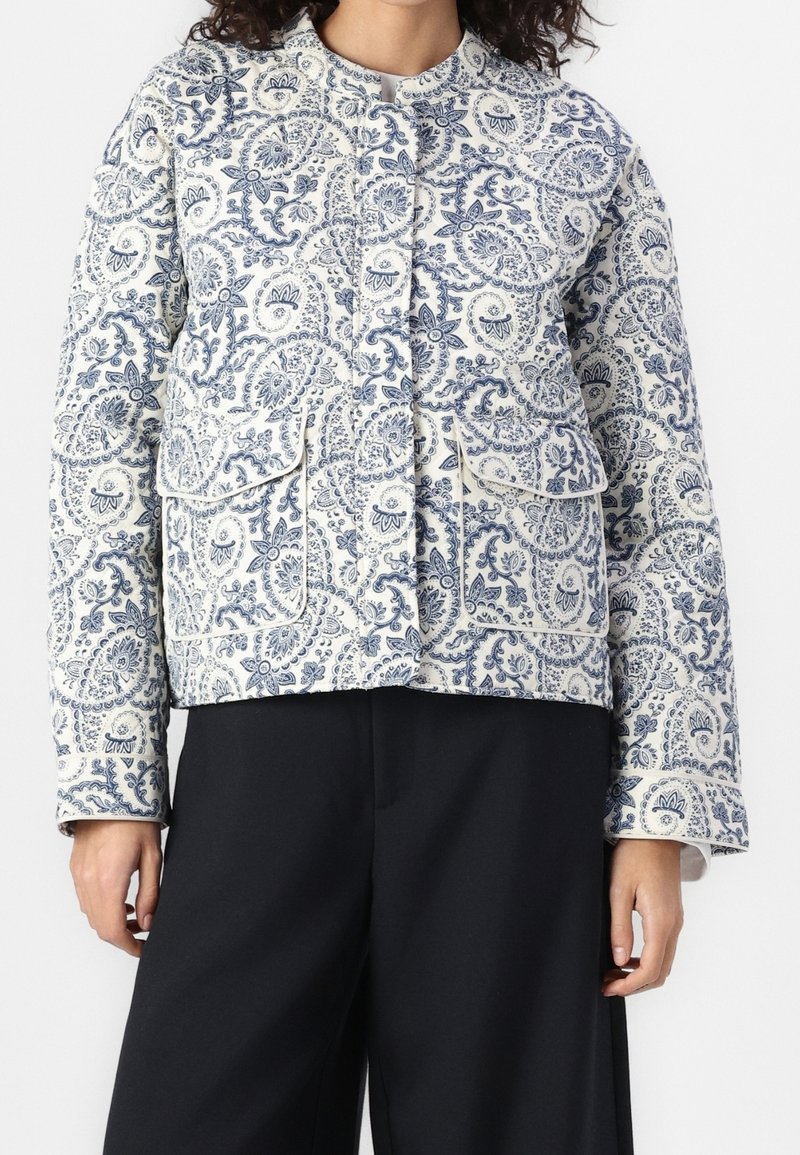 Veste matelassée avec motif cachemire bleu et crème, dotée d'un col rond, de poches avant et d'une coupe décontractée. Tissu texturé avec imprimé détaillé.