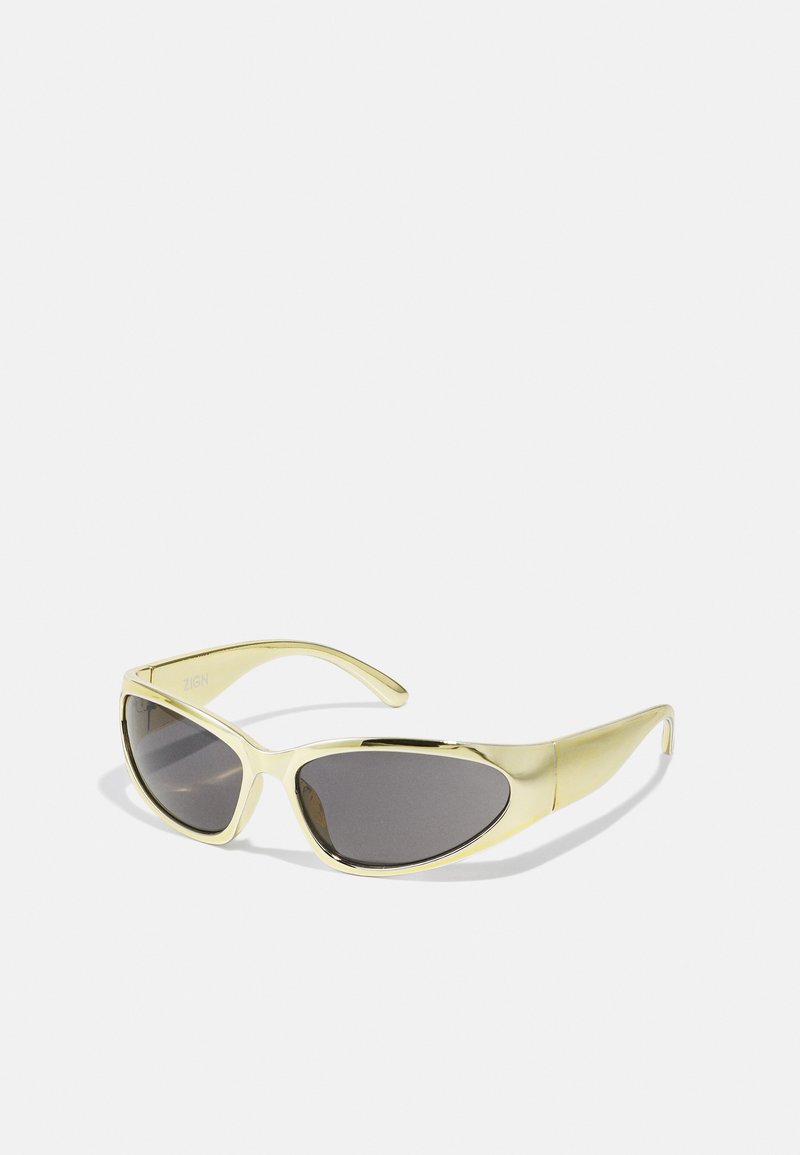 Gele zonnebril met een slank, ovaal frame, donkere getinte lenzen en gebogen pootjes. De afwerking is glanzend met minimale hardwaredetails.