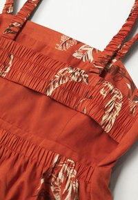 Rotes und beiges, floral gemustertes Kleid mit gerafftem Stoff, dünnen Trägern und einer glatten Textur, das ein lässiges Design unterstreicht.