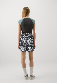 Conjunto casual que incluye una camiseta de manga corta gris oscuro y azul verdoso y pantalones cortos negros con un patrón abstracto en blanco. Combinado con calcetines y zapatos blancos.