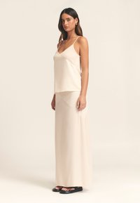 Lichtbeige satijnen camisole met dunne bandjes, gecombineerd met een bijpassende lange rok. De stof heeft een gladde textuur en minimale ontwerpelementen.